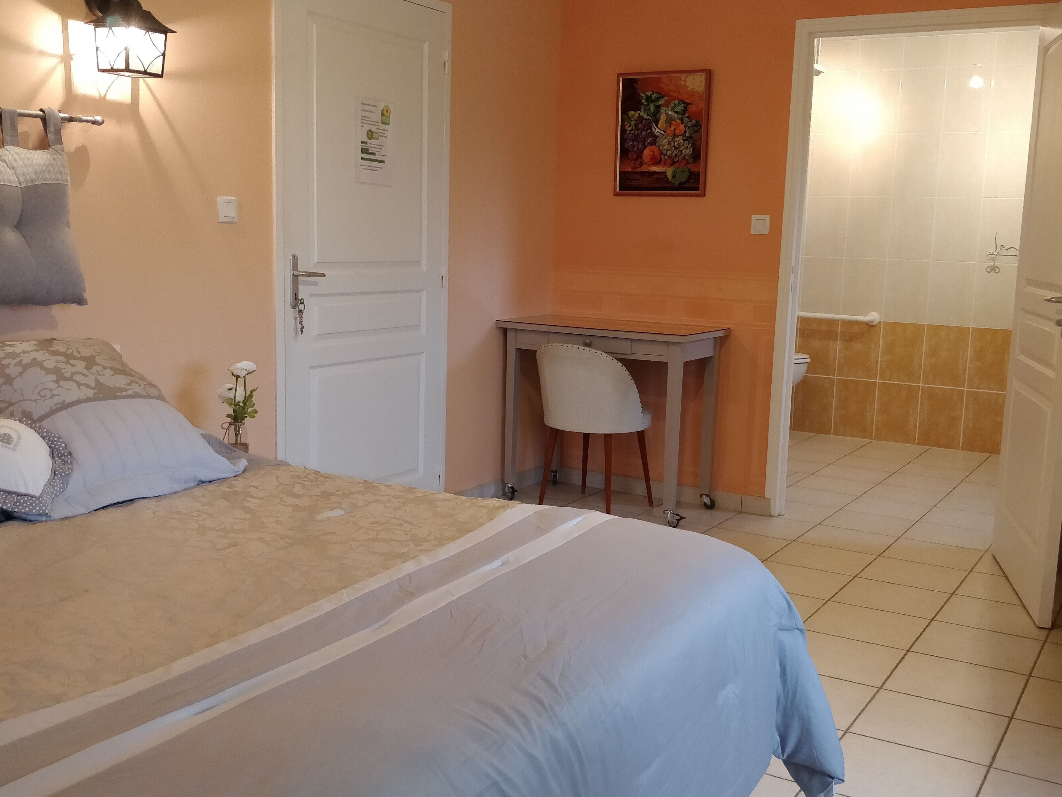 Une chambre avec un lit, un bureau et une chaise. Il y a une porte avec une pancarte et un tableau au mur.