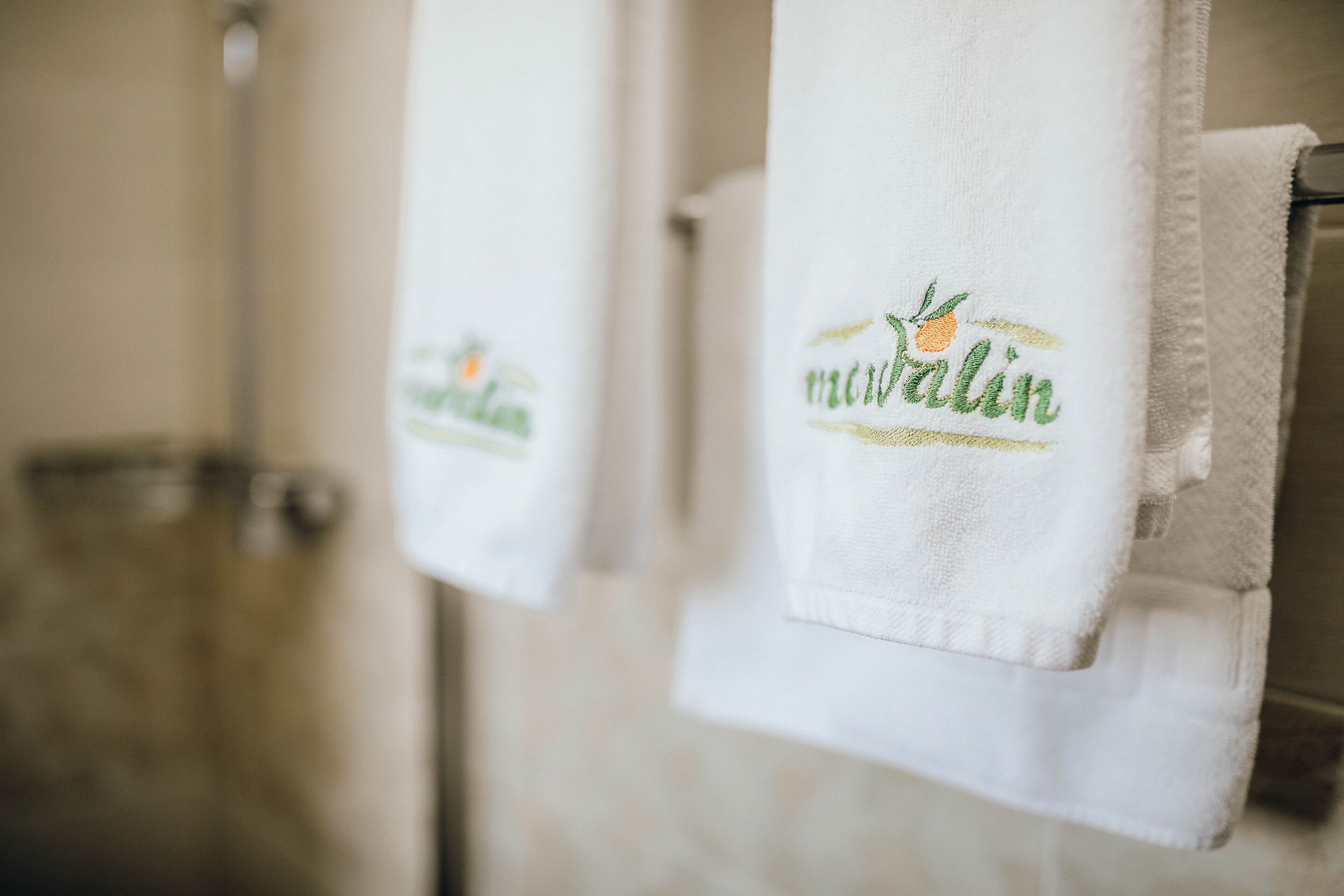Two white towels hanging on a rack with embroidered text and a logo.