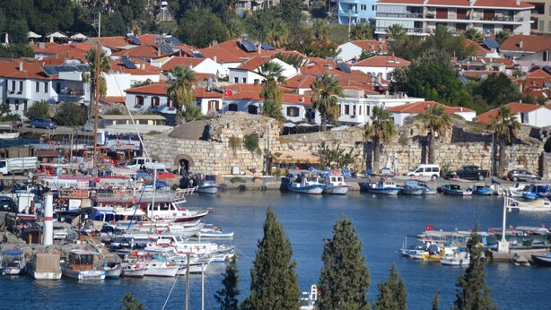 A marina with numerous boats docked, surrounded by residential buildings with red-tiled roofs and stone walls. - Mandalin Pansiyon (Seferihisar)