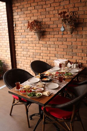 A dining table set with plates, bowls, and glasses, surrounded by wicker chairs with red cushions.