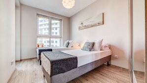 A modern bedroom with a large bed, a smaller bed, and a window with a view of buildings. - Rint - Centrum Kaczorowskiego (Bialystok)
