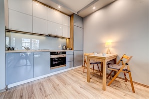 A modern kitchen with grey cabinets, a wooden dining table, and a chair. - Rint - Centrum Kaczorowskiego (Bialystok)