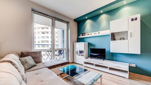 A modern living room with a sofa, a glass coffee table, a TV, and built-in cabinets. - Rint - Centrum Kaczorowskiego (Bialystok)