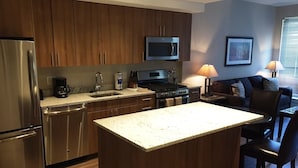 A modern kitchen with wooden cabinets, stainless steel appliances, a central island, and a dining area with a table and chairs. - Weichert Suites at The Bartlett (Arlington)