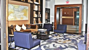 A lobby with a blue sofa set, a glass coffee table, a patterned rug, and a bookshelf with various items. - Weichert Suites at The Bartlett (Arlington)