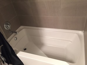 A bathroom with a white bathtub, a showerhead, and a drain. - Weichert Suites at The Bartlett (Arlington)