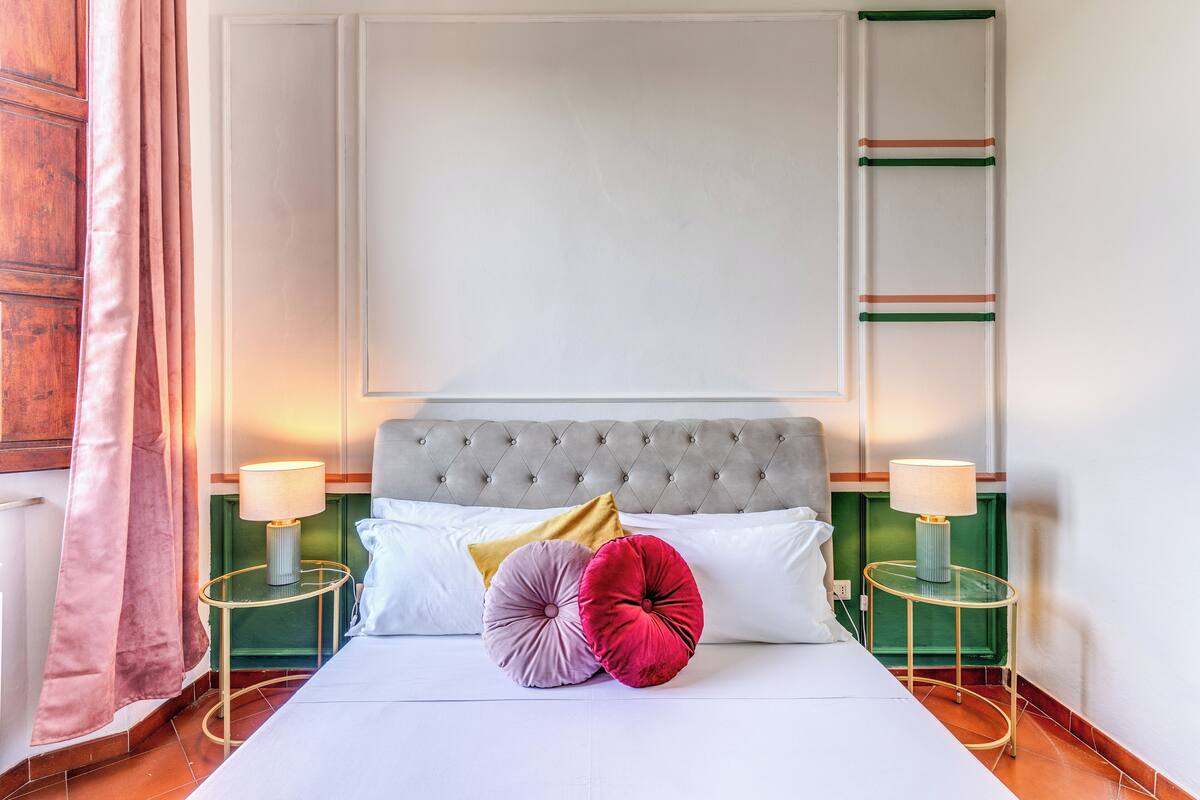 A hotel room with a tufted headboard, two bedside tables with lamps, a bed with white linens, and a green accent wall.