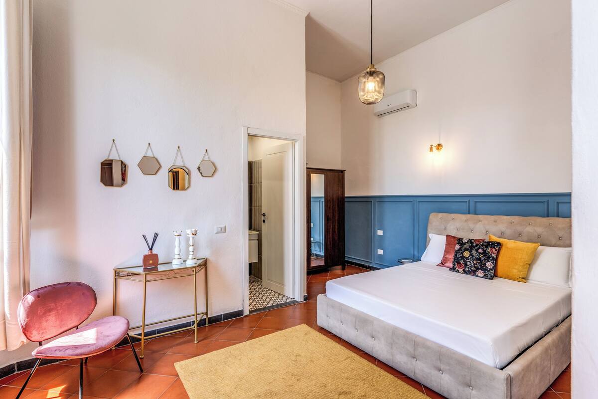 A bedroom with a bed, a desk, and a chair. There is a door leading to another room.