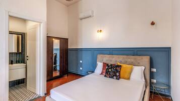 A bedroom with a large bed, a wooden wardrobe, a bathroom with a mirror, and a small round table.