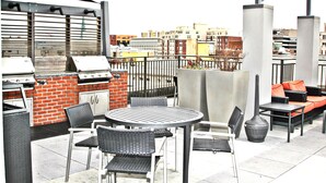 An outdoor patio with a grill, wicker furniture, and a view of the cityscape. - Weichert Suites at Thomas Circle (Washington)