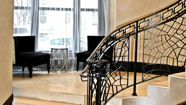 A staircase with a black metal railing, leading to a landing with a bench and a small table. - Weichert Suites at Thomas Circle (Washington)