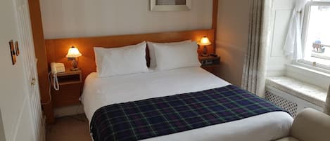 A neatly made bed with a plaid blanket, two bedside lamps, and a telephone on a bedside table.