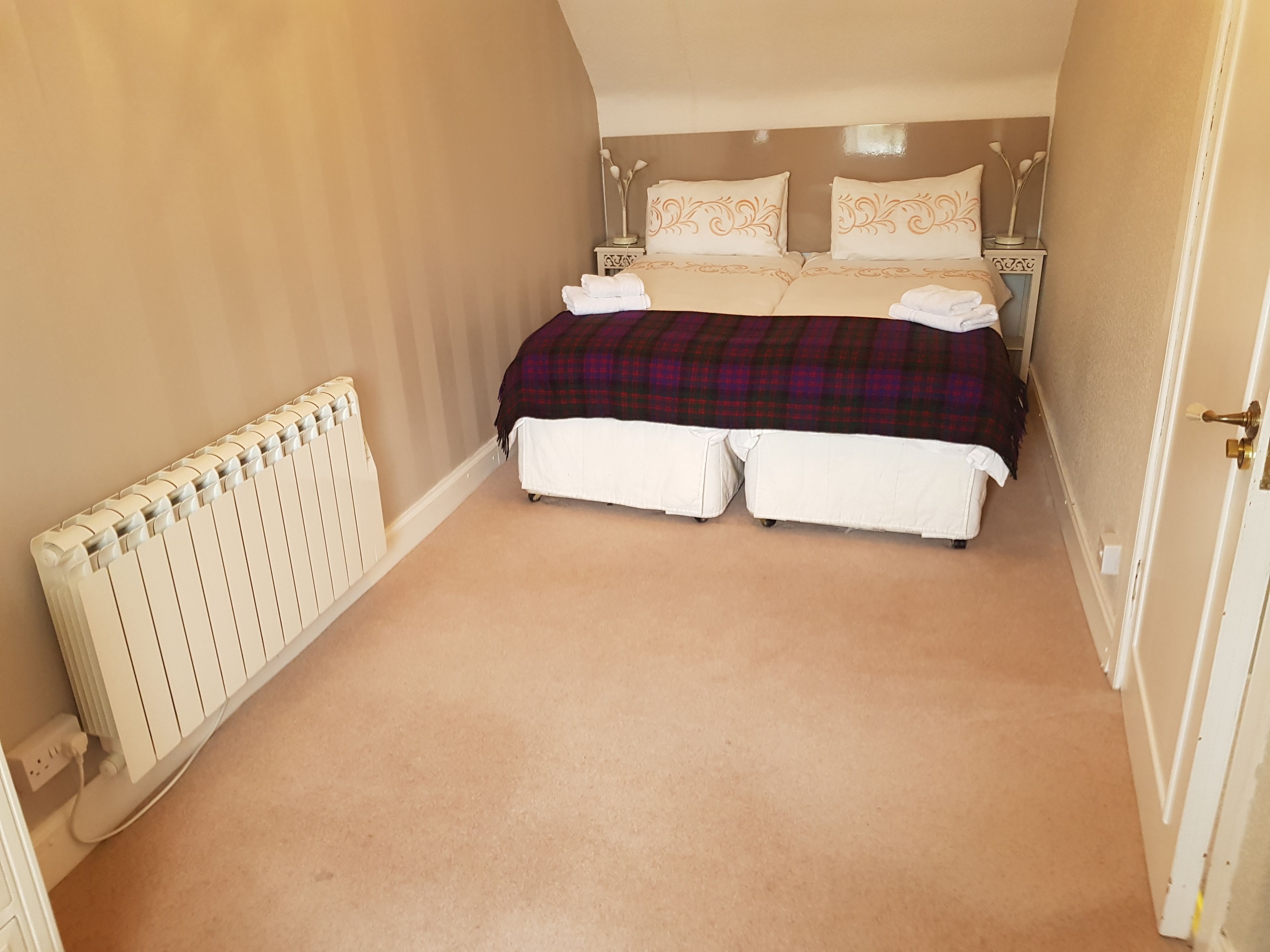A bedroom with a double bed, two bedside tables, a radiator, and a door.