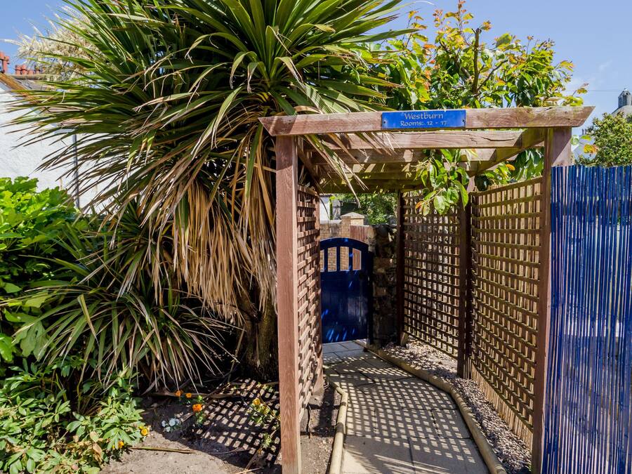 Una entrada al jardín con un pérgola de madera, una verja azul y un cartel que indica 'Westburn'.