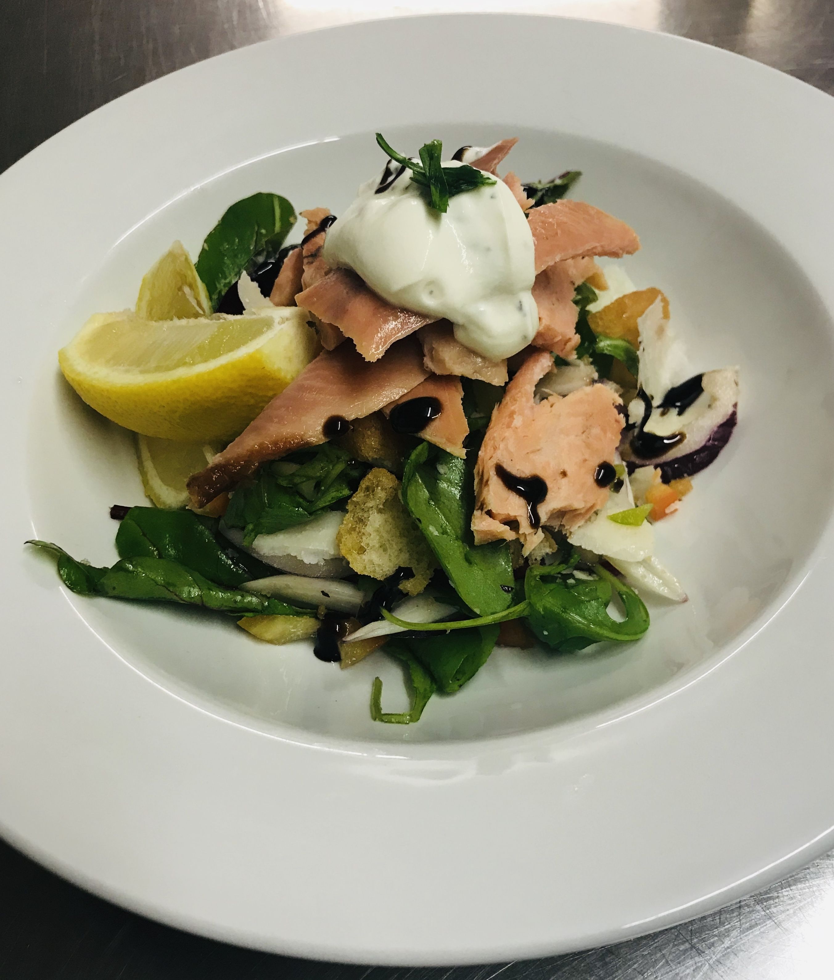 A plate of food with salmon, greens, and lemon slices.