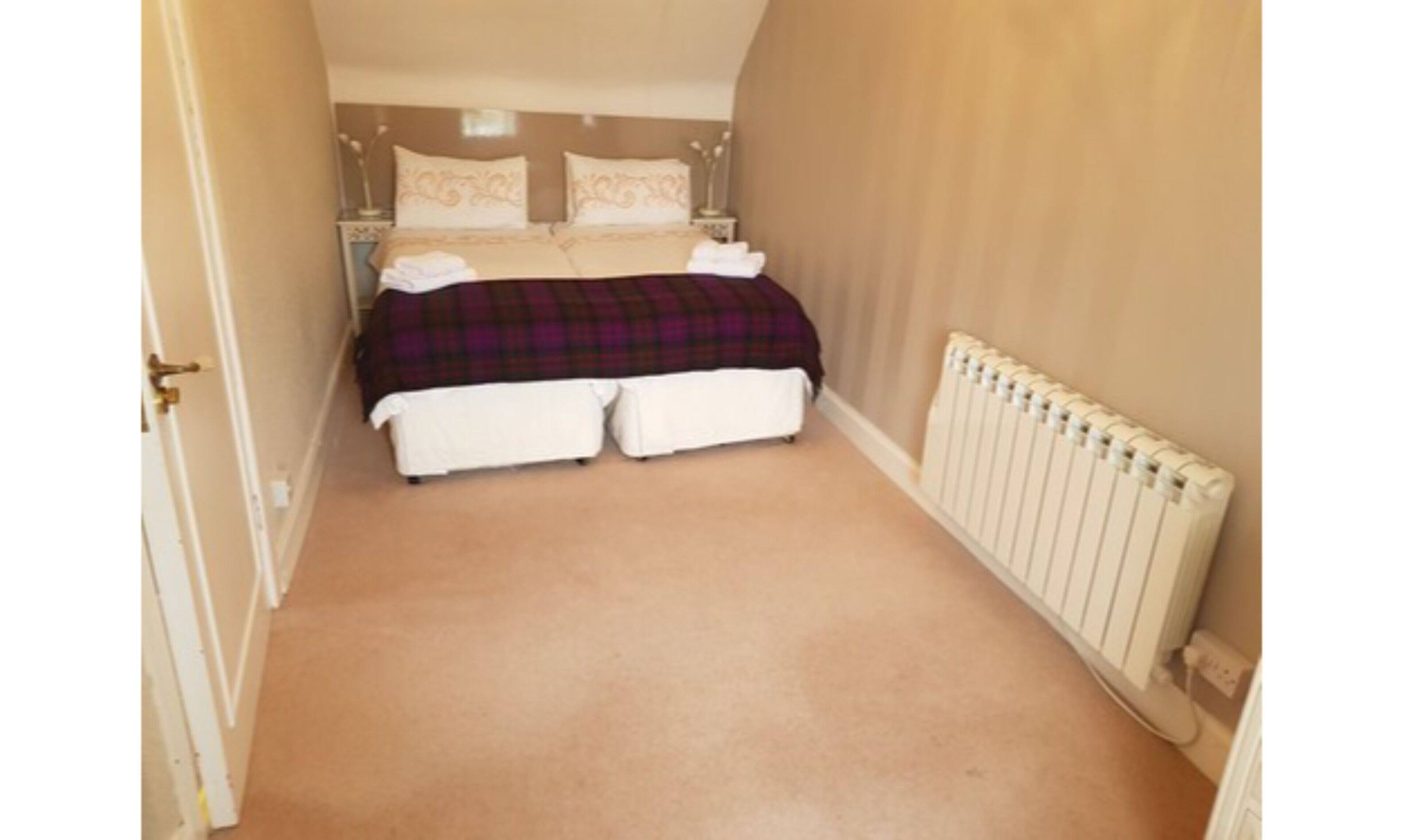 Une chambre avec un lit double, un radiateur et un sol recouvert de moquette.