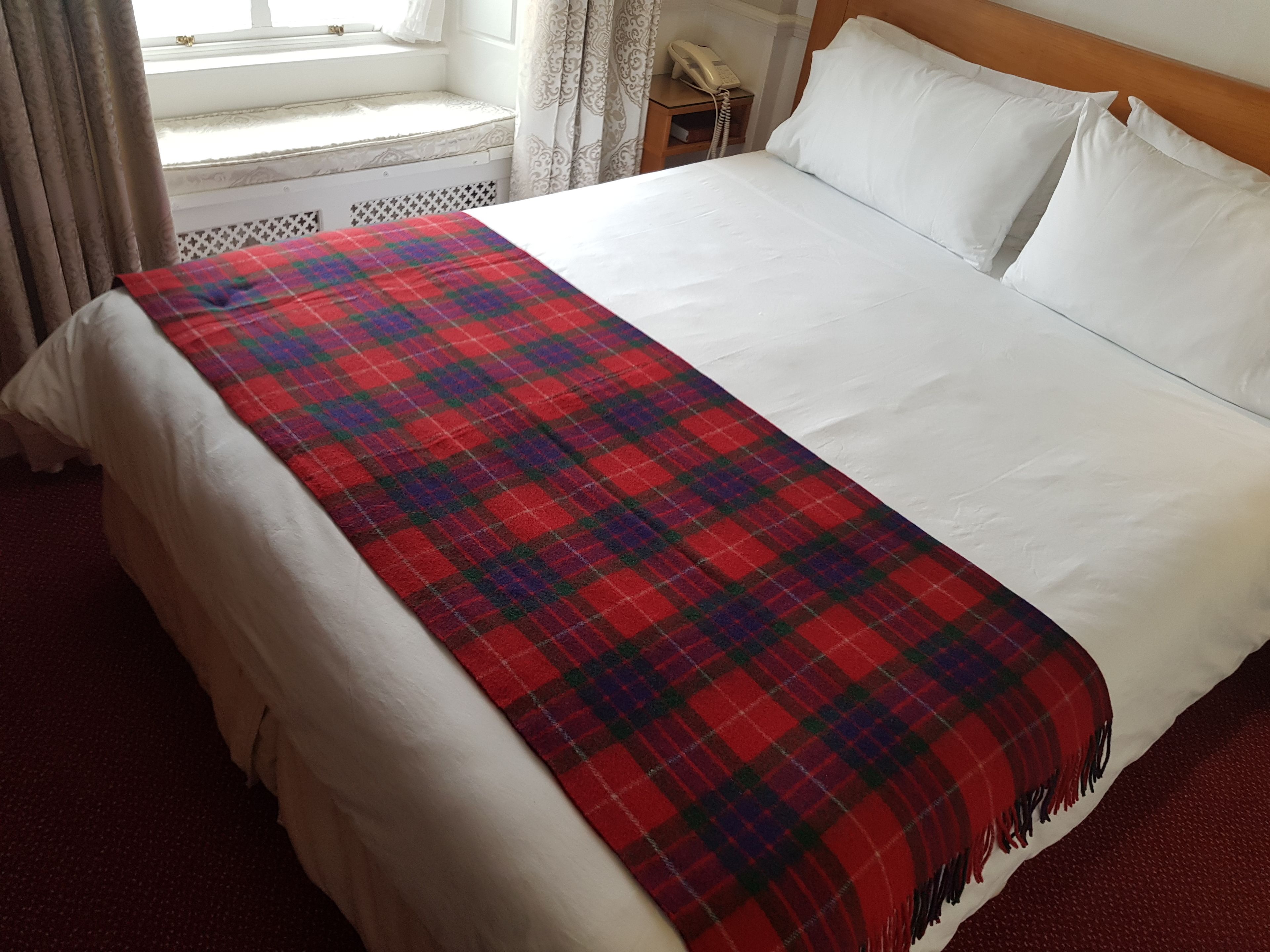 A neatly made bed with a plaid blanket, white pillows, and a wooden headboard.