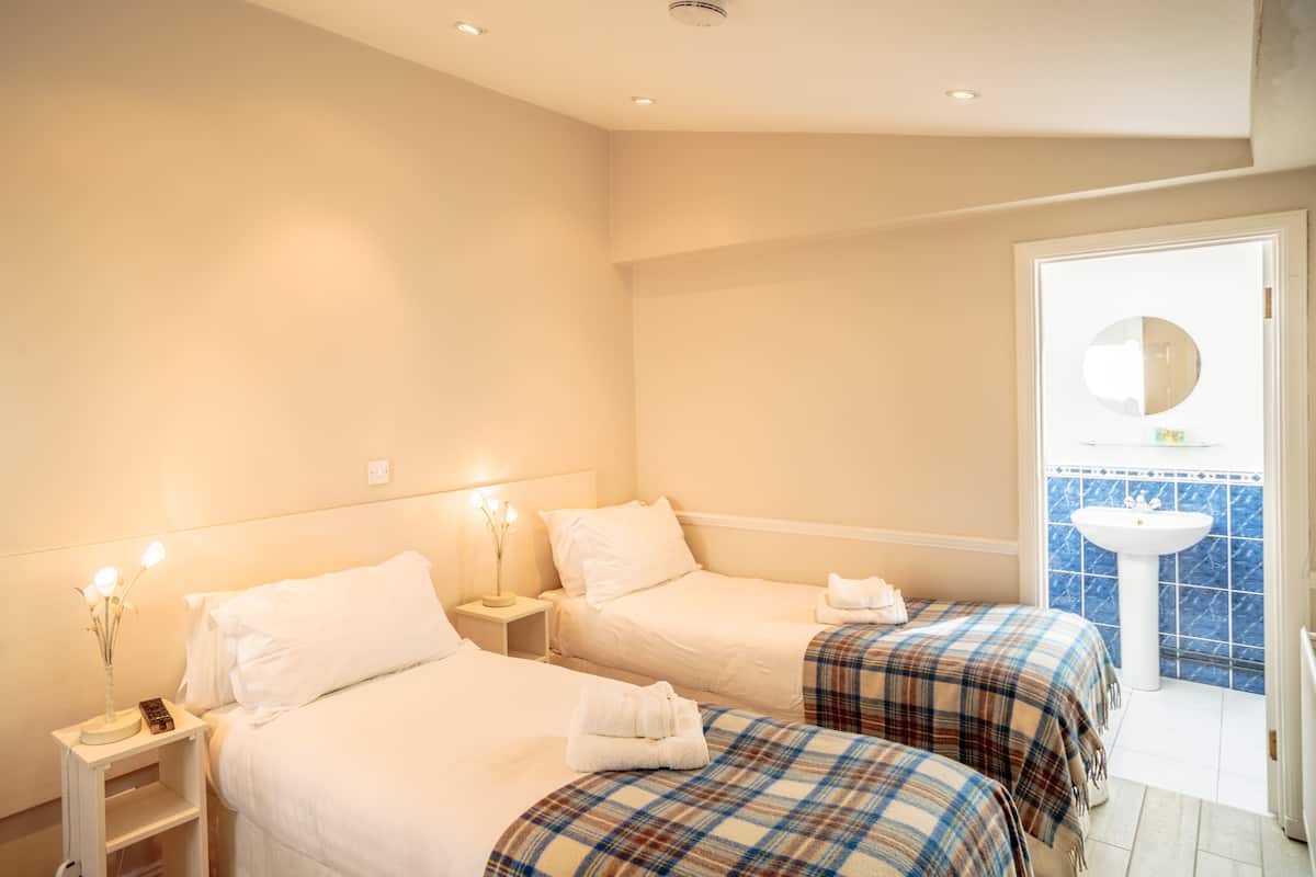 Une chambre d’hôtel avec deux lits, une table de chevet avec une lampe, une salle de bain avec un lavabo et un miroir, et un balcon avec vue.