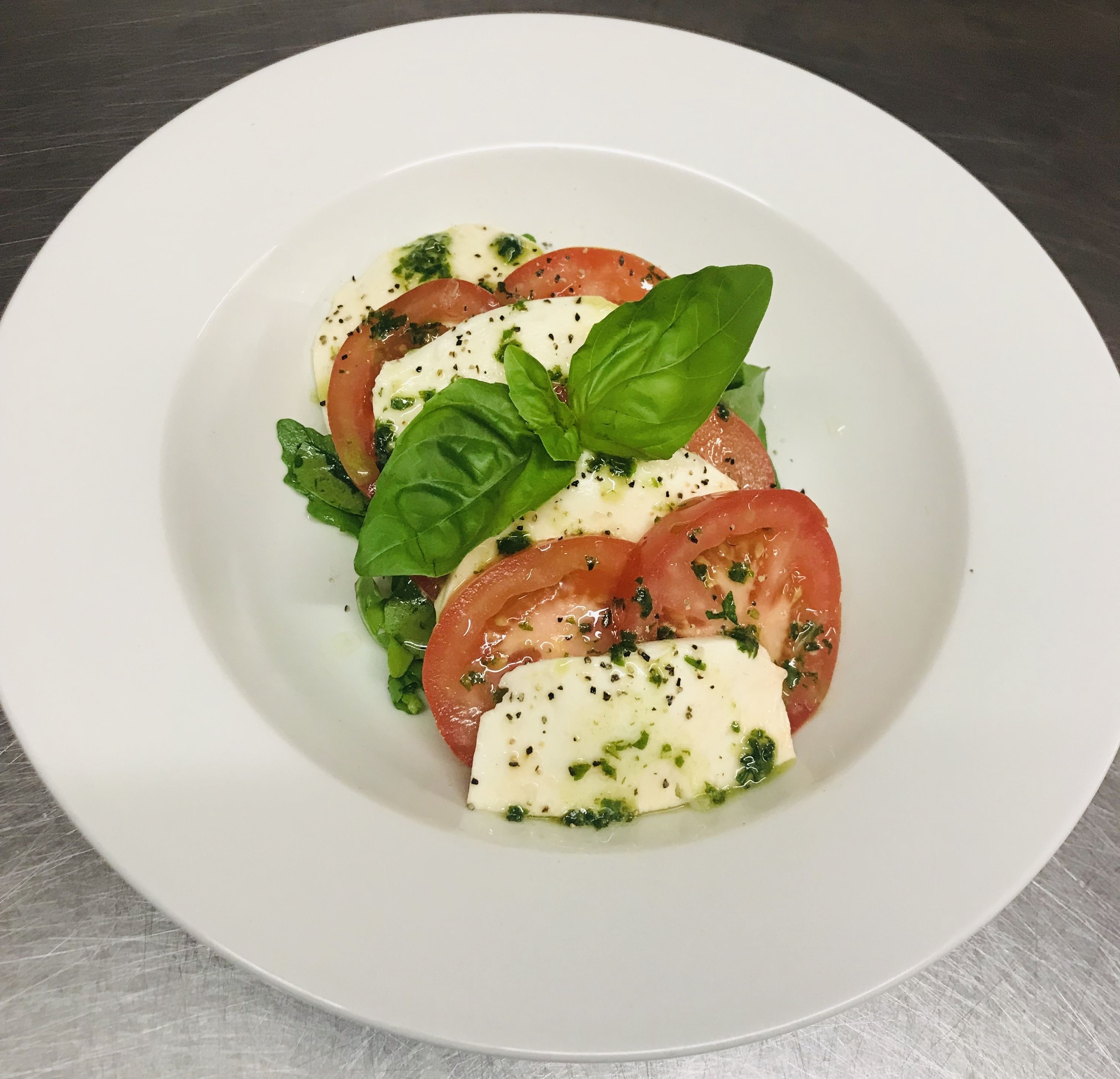 A white plate with a salad of tomatoes, cheese, and basil.