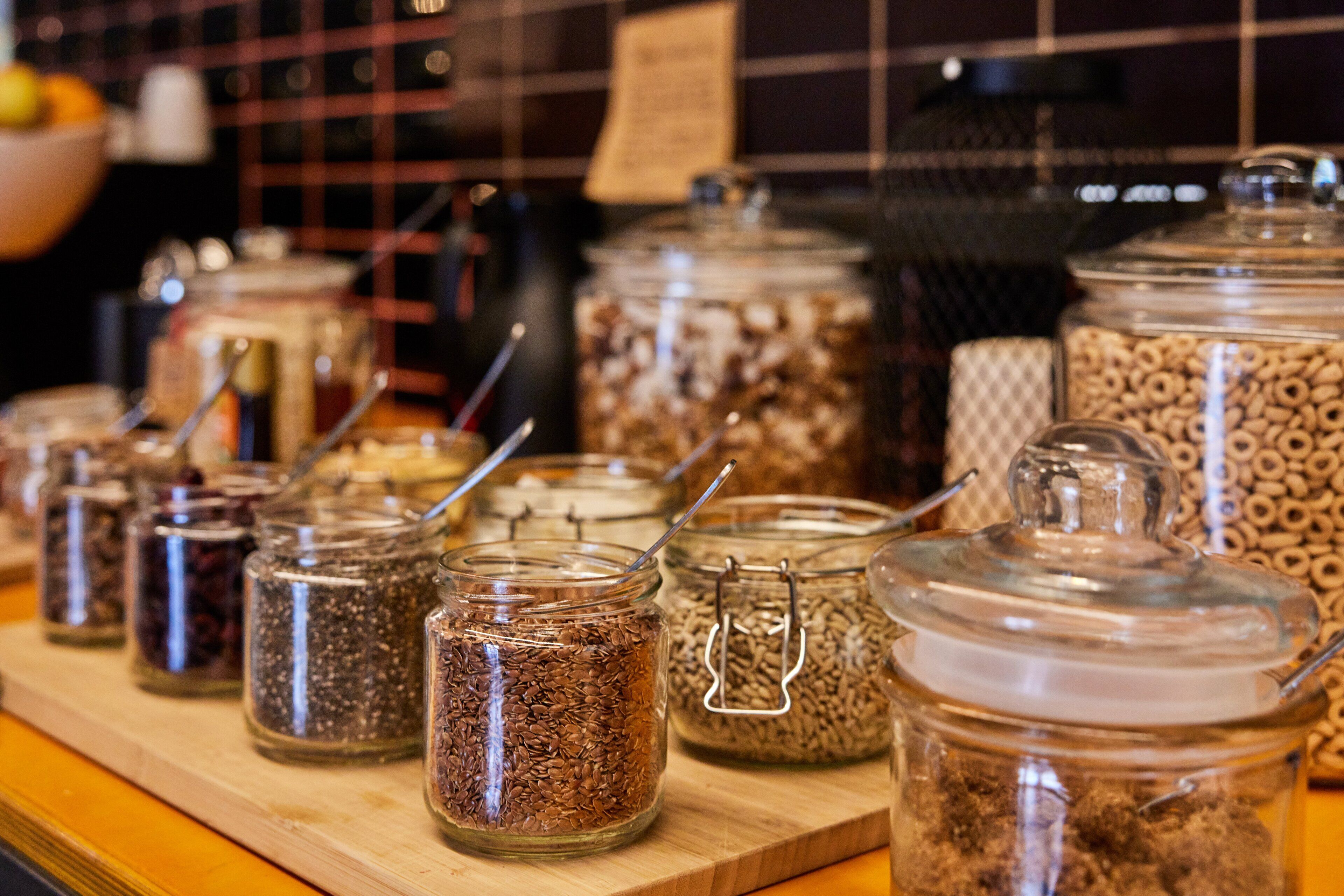 A variety of glass jars with metal clasps containing different grains and seeds, arranged on a wooden surface.