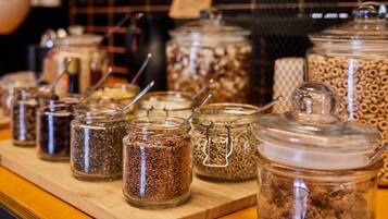 A variety of glass jars with metal clasps containing different grains and seeds, arranged on a wooden surface.