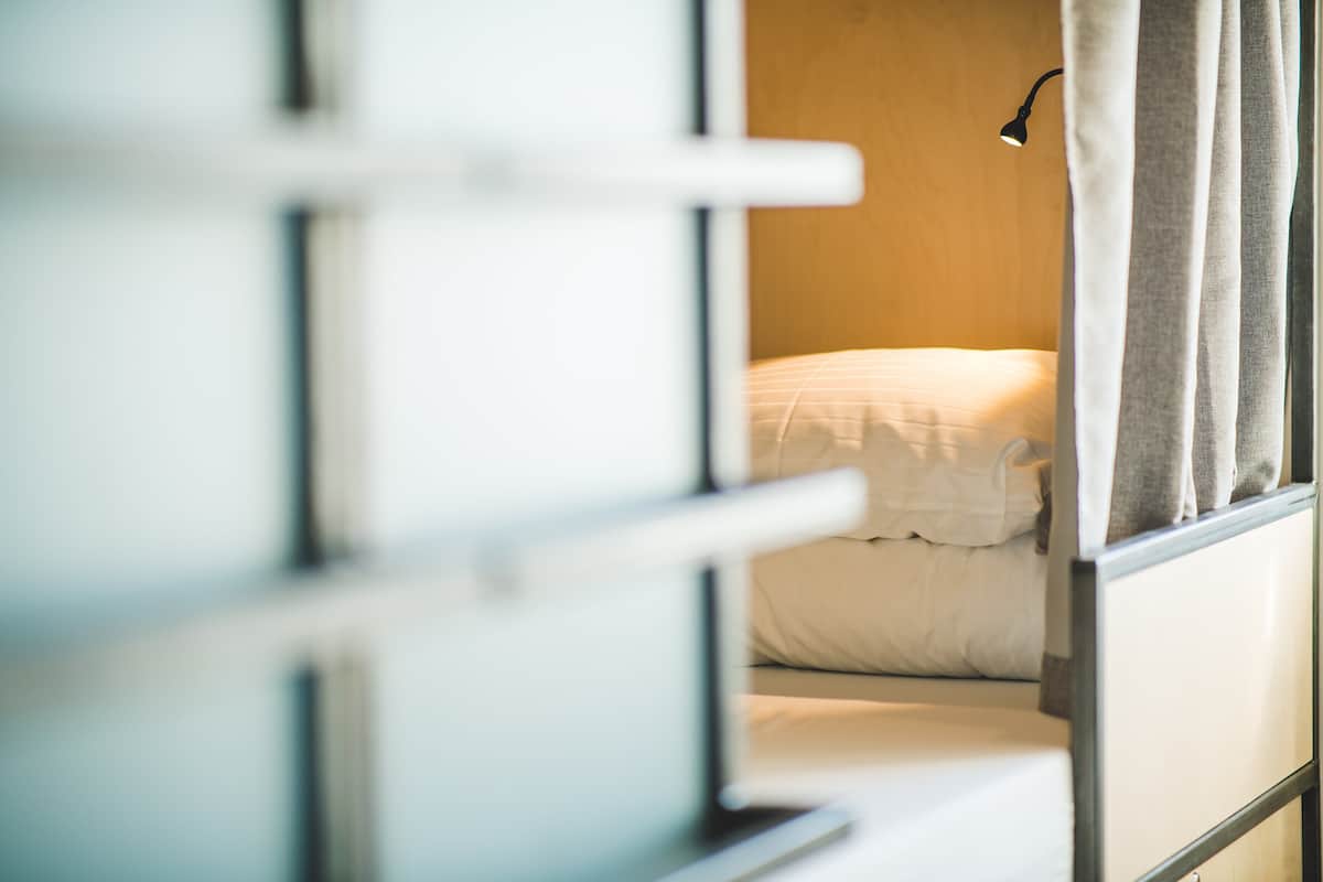 A room with a bed, a window with curtains, and a wall-mounted lamp.