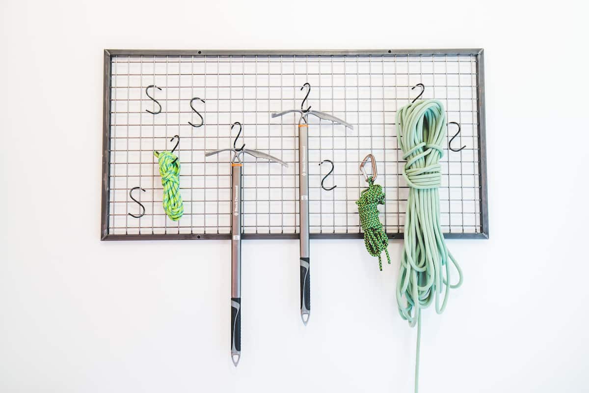 A pegboard with numbered hooks holding various items like a green garden hose, a green and black rope, and two metal tools.
