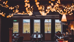 A restaurant with a long table, multiple chairs, and a view of the outdoors through large windows. - Midgard Base Camp (Rangárþing eystra)