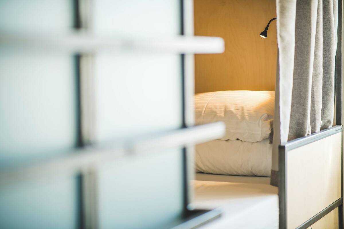 A room with a bed, a window with curtains, and a wall-mounted lamp.