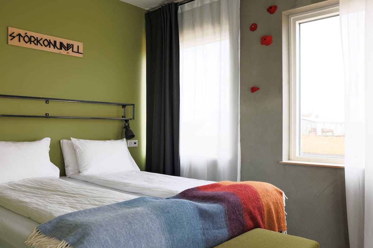 A hotel room with a bed, a colorful blanket, a sign on the wall, and a window with curtains.