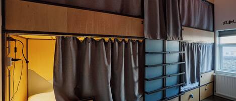 A dormitory room with bunk beds, curtains, a radiator, and a window with a view.