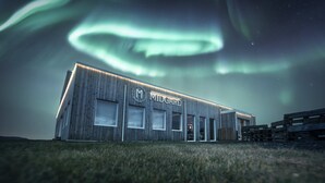 A modern building with the sign "MIDGARD 1" under a night sky with the Northern Lights. - Midgard Base Camp (Rangárþing eystra)