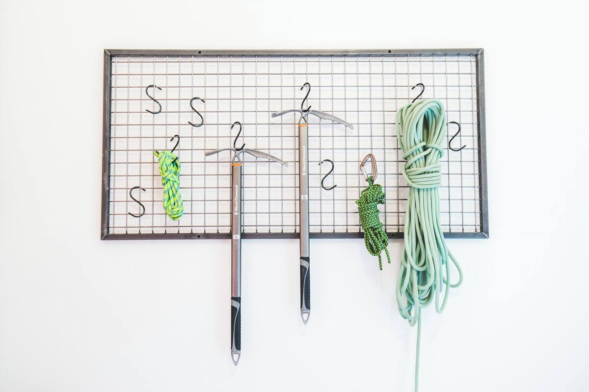 A pegboard with numbered hooks holding various items like a green garden hose, a green and black rope, and two metal tools.