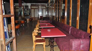 Un restaurante con mesas y sillas de madera, un banco acolchado rojo y grandes ventanales.