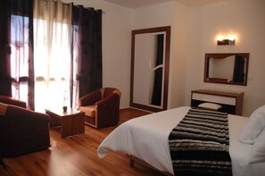 A hotel room with a bed, a chair, a small table, a mirror, and a window with curtains.