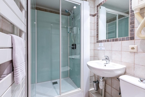 Un bany modern amb dutxa de vidre, un lavabo blanc i un mirall sobre el lavabo.