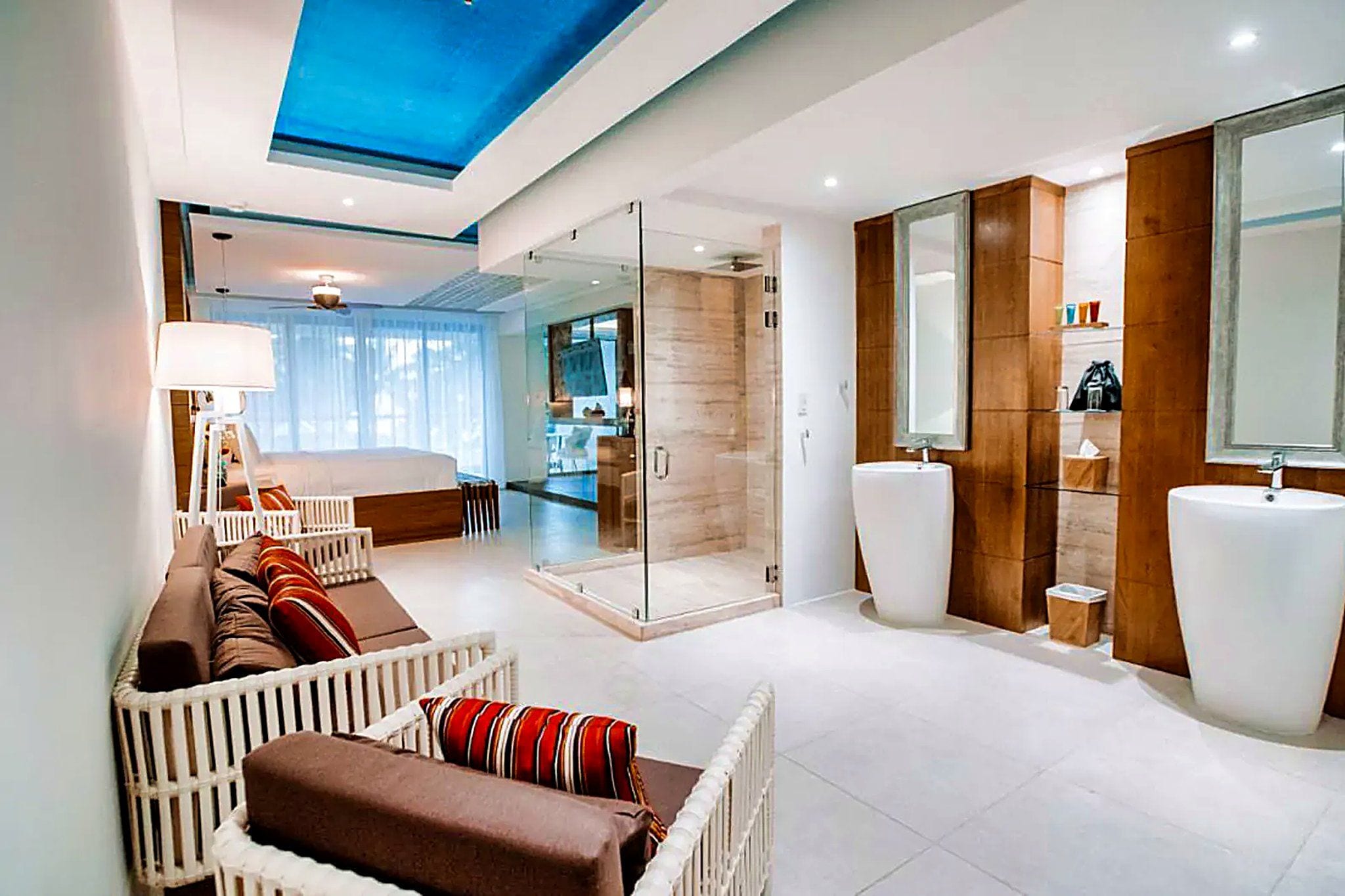 Una habitación de hotel moderna con ducha de vidrio, un sofá, una cama y un espejo grande.