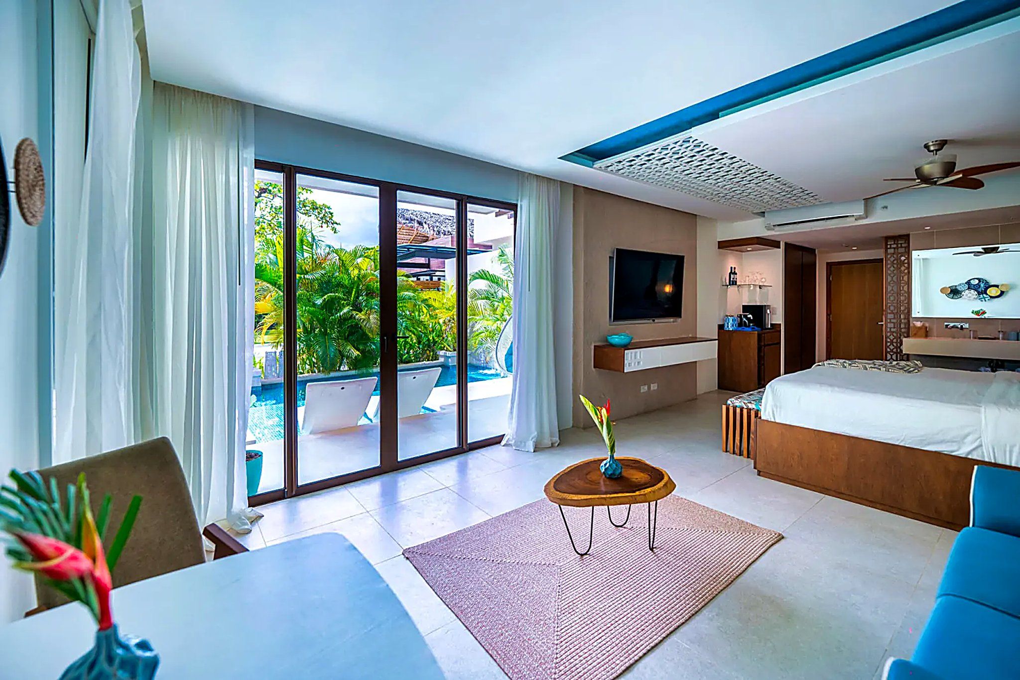 A hotel room with a large sliding glass door to a pool, a bed, a desk, and a TV.