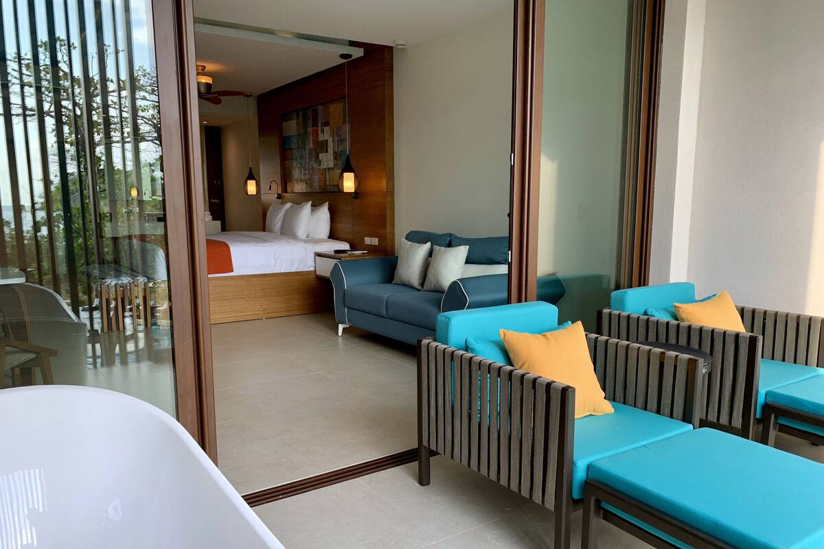 A modern hotel room with a bed, a blue sofa, and a lounge area with striped chairs.