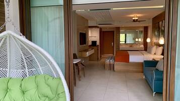 Habitación de hotel con una silla verde acolchada, un sofá azul, una mesita, un escritorio con una computadora y un baño con espejo y lavamanos.