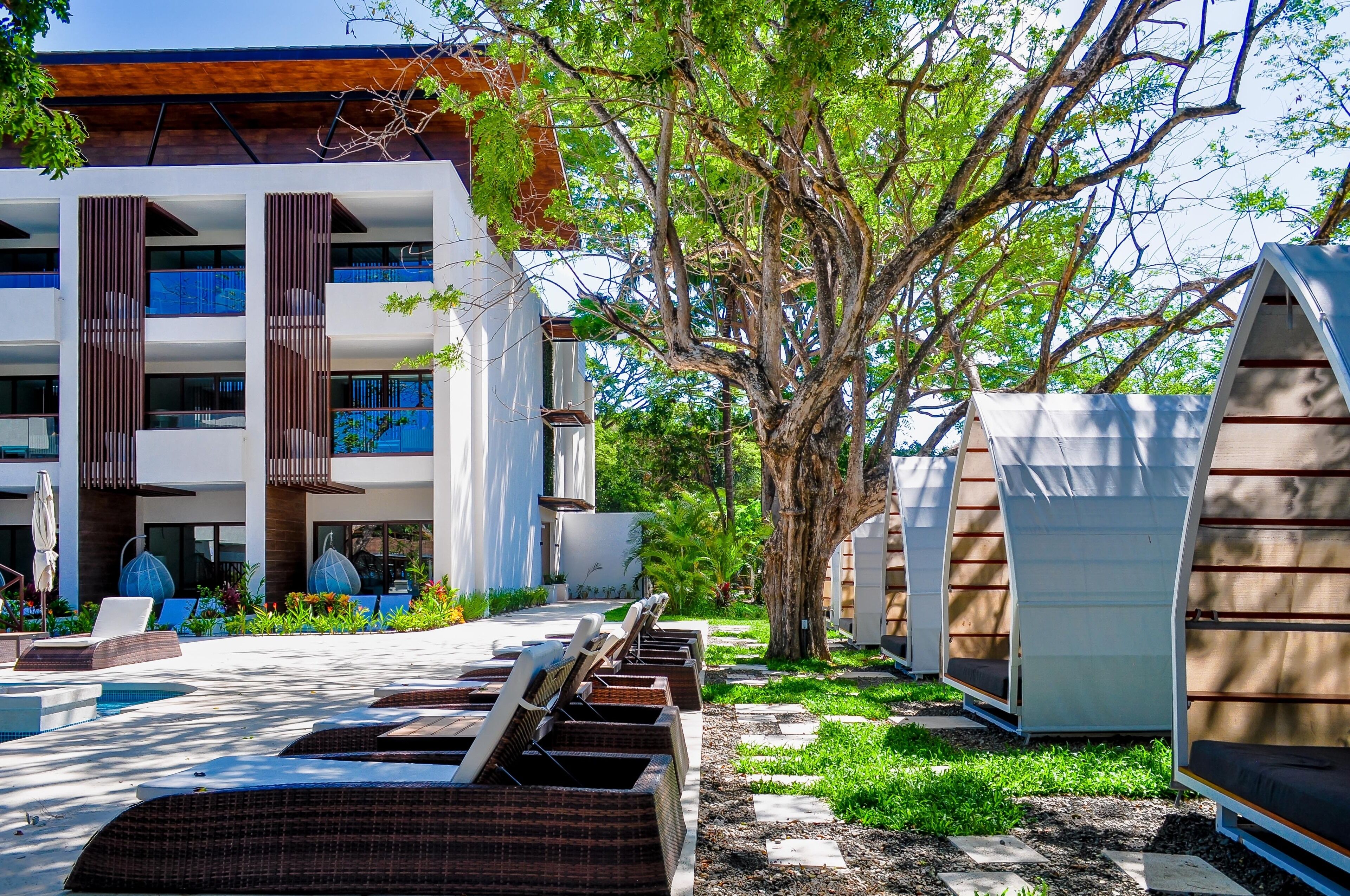 A modern building with multiple balconies, outdoor seating, and a tree in the center.