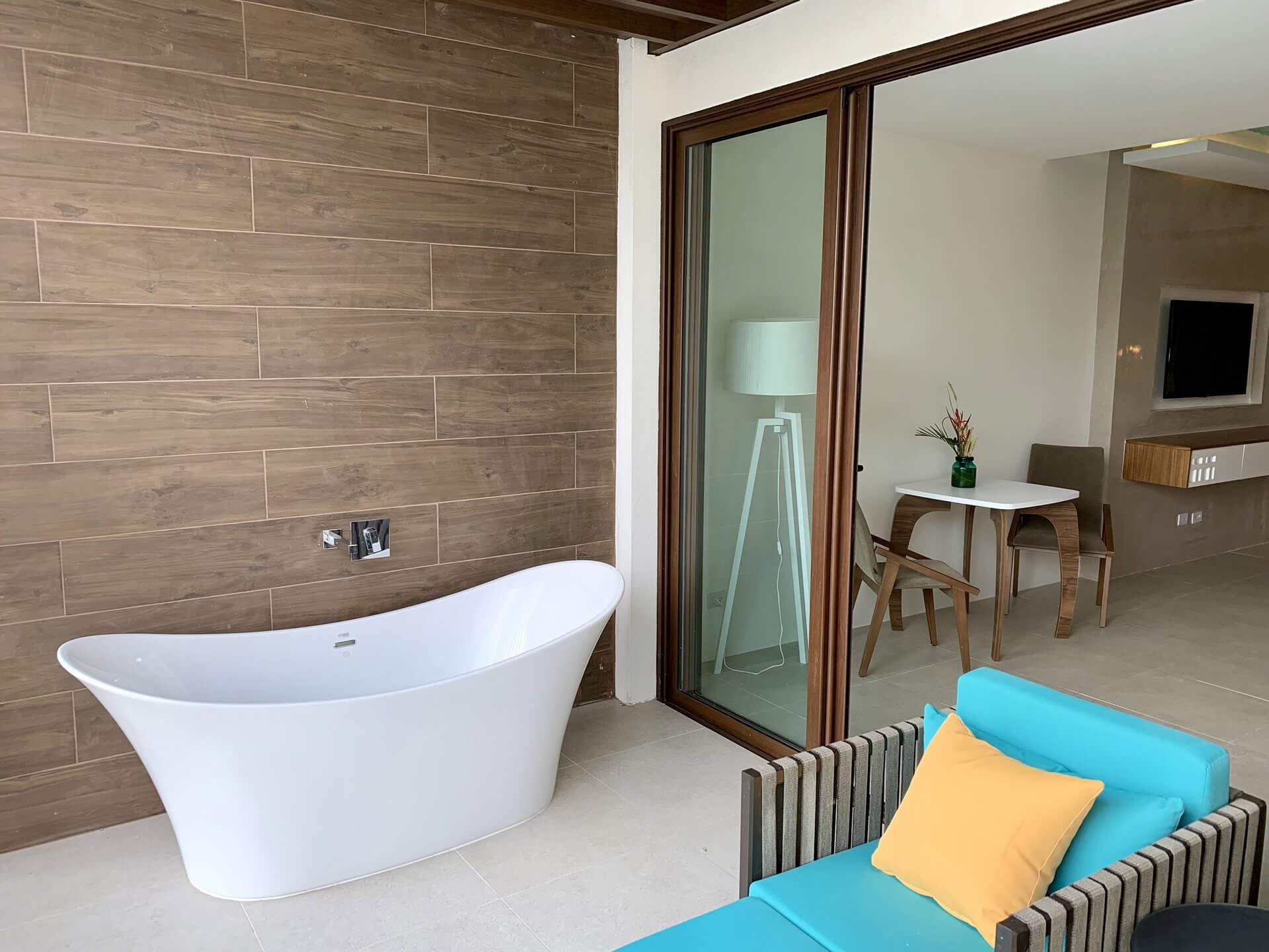 A modern bathroom with a freestanding bathtub, a glass shower enclosure, and a seating area with a blue sofa and a yellow pillow.