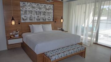 Una cama grande con cabecera de madera, una mesita de noche con una botella y un vaso, y un banco con un cubrecolchón estampado.