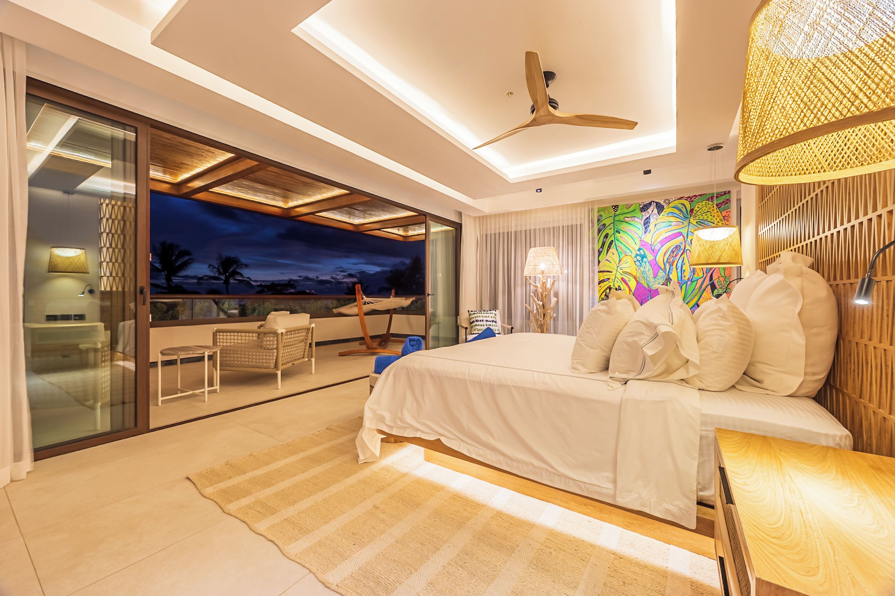 A modern hotel room with a large bed, a balcony with a view, and a ceiling fan.
