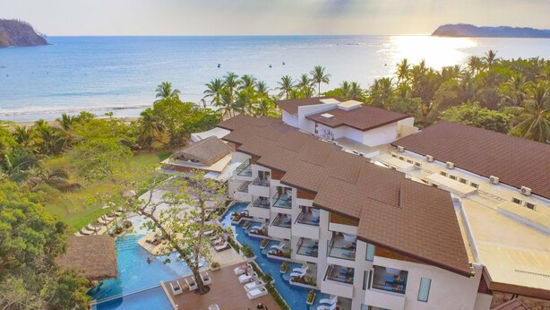 A resort with a swimming pool, multiple buildings, and a view of the ocean. - Azura Beach Resort - All Inclusive - Adults Only (Sámara)
