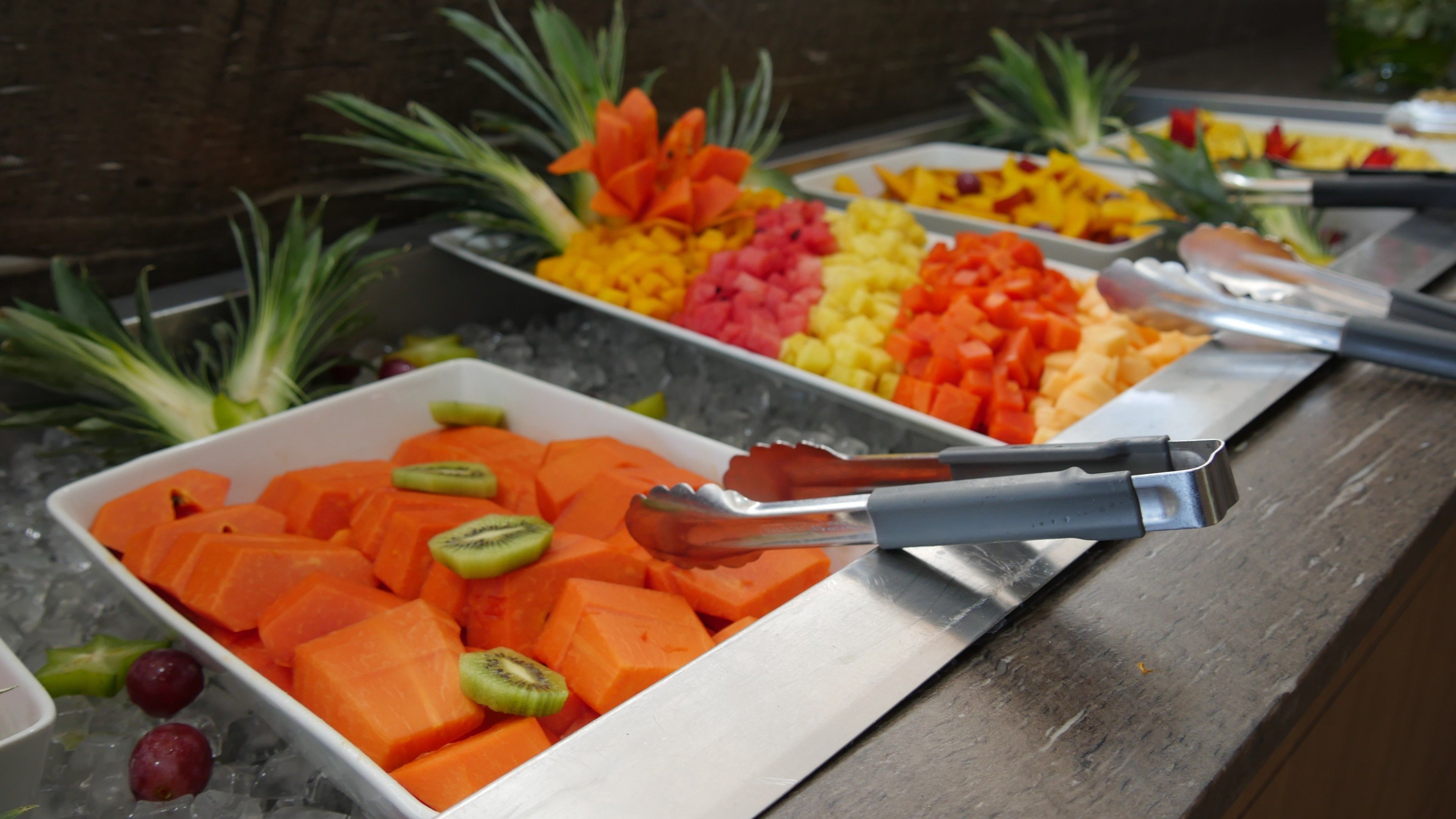 Un bufé con diversas frutas y verduras, incluyendo zanahorias y rodajas de kiwi, dispuestas sobre una bandeja de metal.