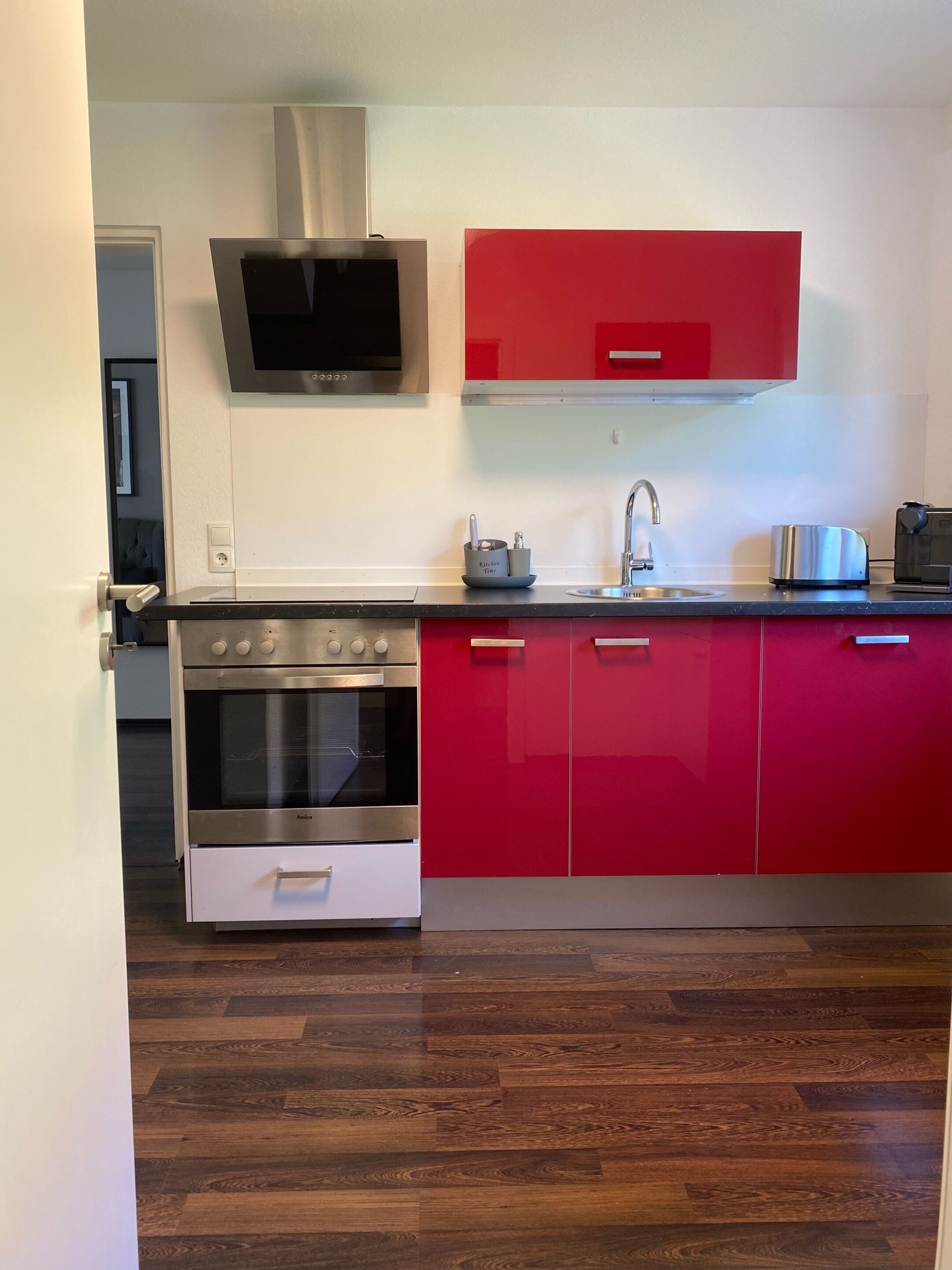 A modern kitchen with stainless steel appliances, red cabinets, and a flat-screen TV mounted above the oven.
