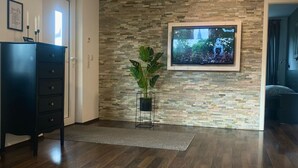 A modern living room with a stone wall, a flat-screen TV, a wooden coffee table, and a dark-colored cabinet.