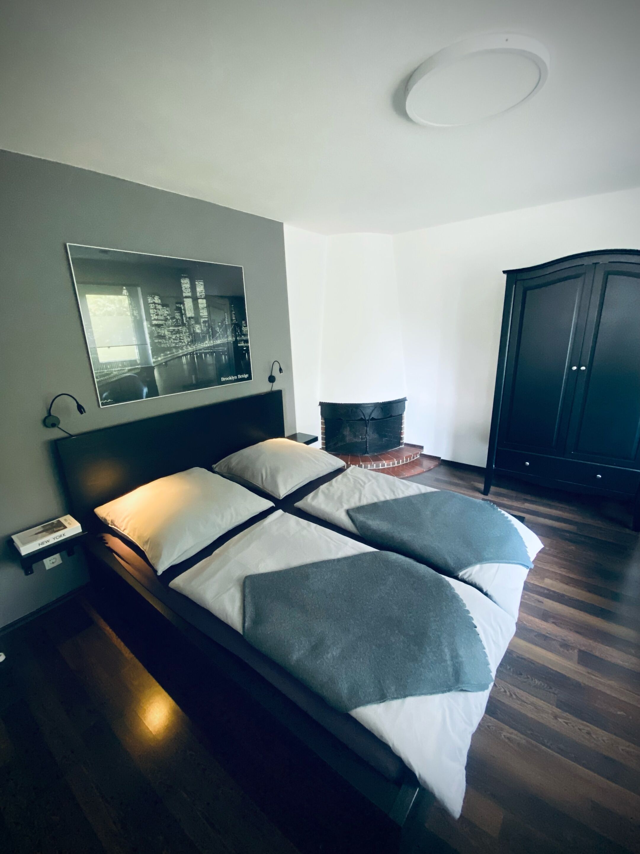 Una camera da letto moderna con un letto, un comodino, una testiera, un quadro appeso al muro, un armadio e una lampada a soffitto circolare.