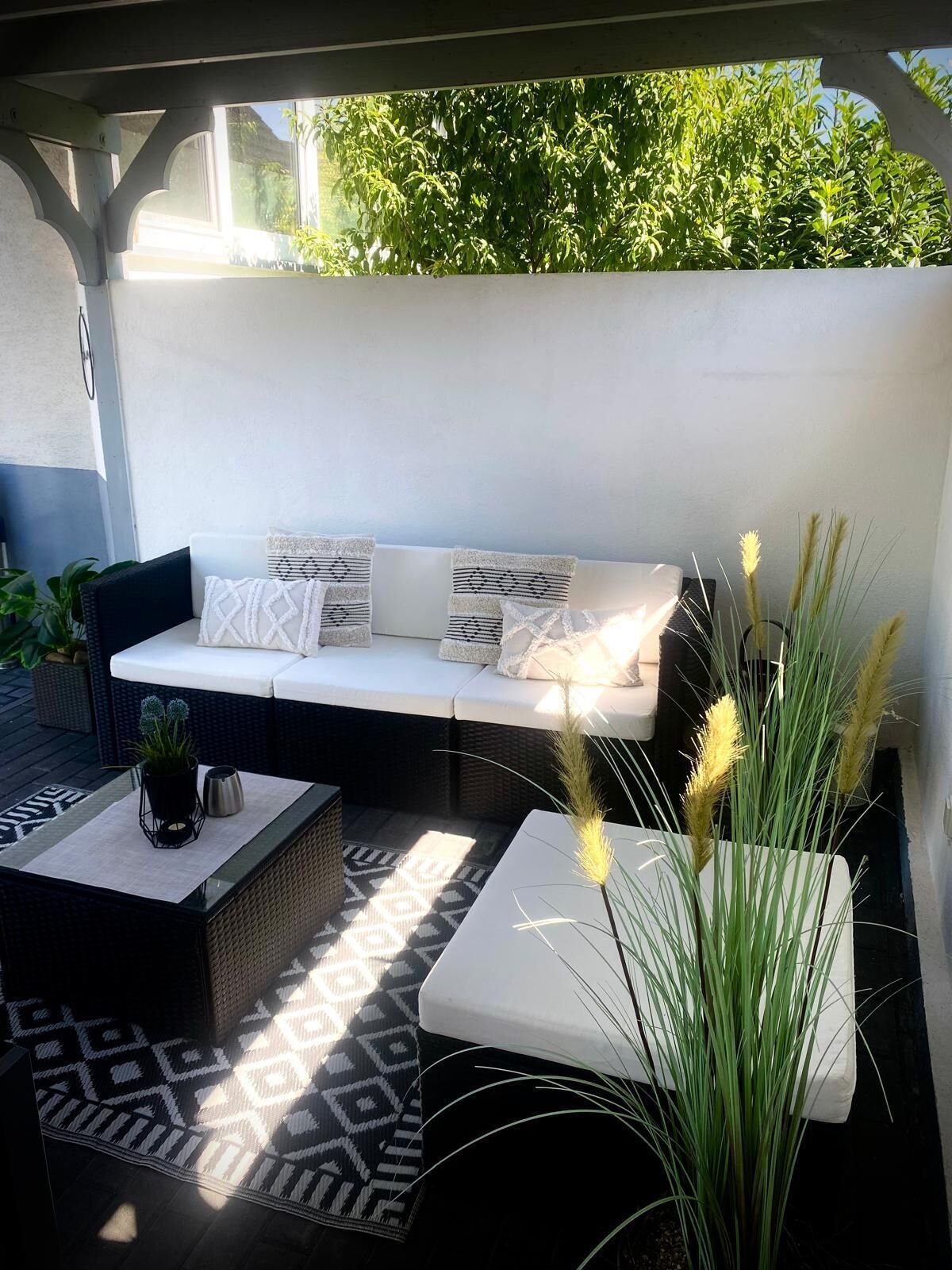 Un espace extérieur aménagé, abrité et doté d’un canapé, de coussins et de jardinières.